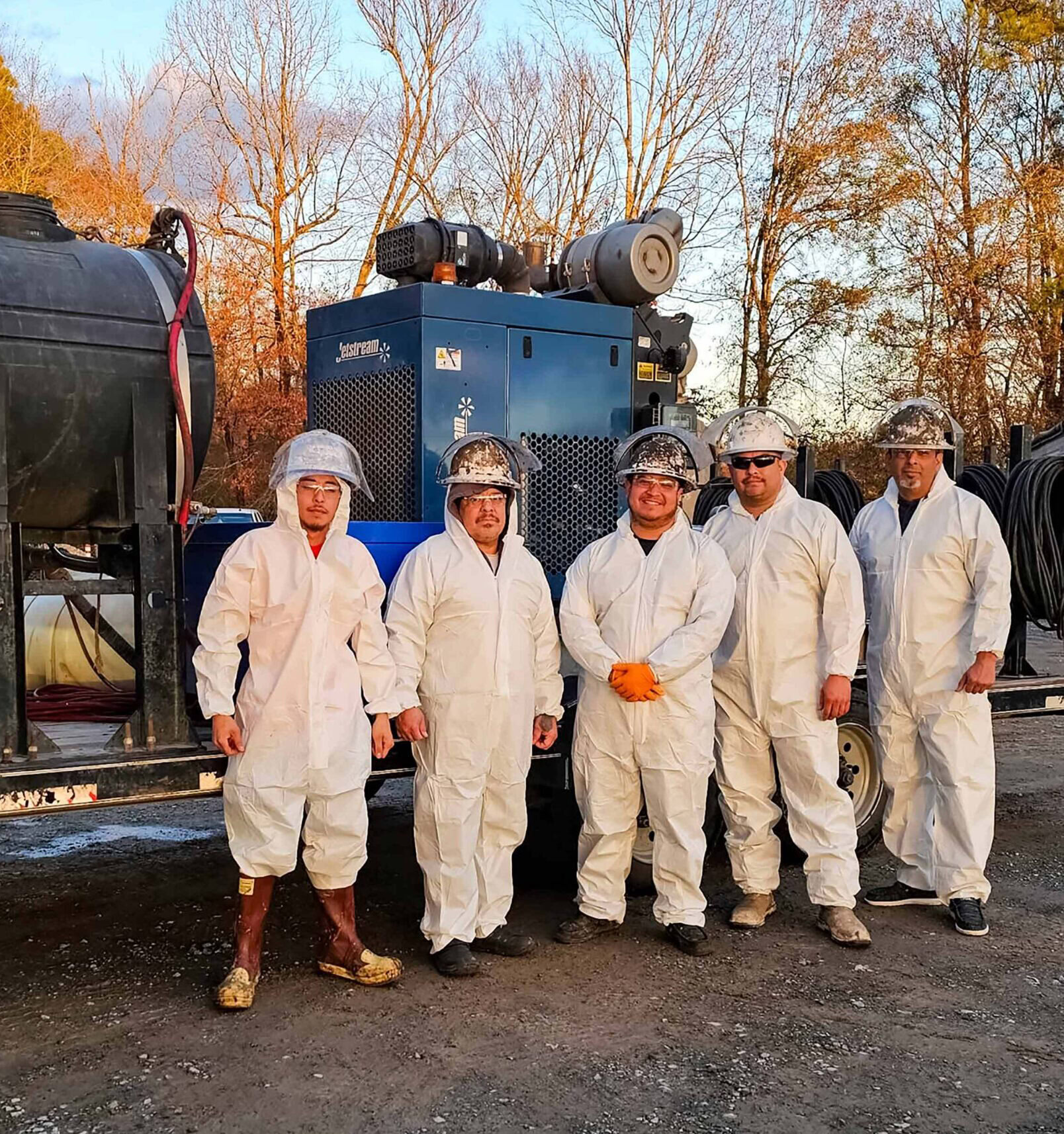 Five men in white coveralls standing next to a truck.