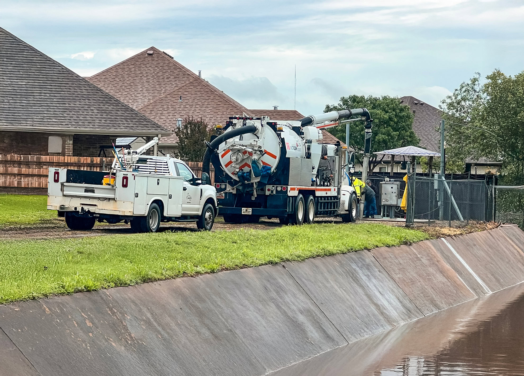 A truck is parked next to a canal with a house on the other side.