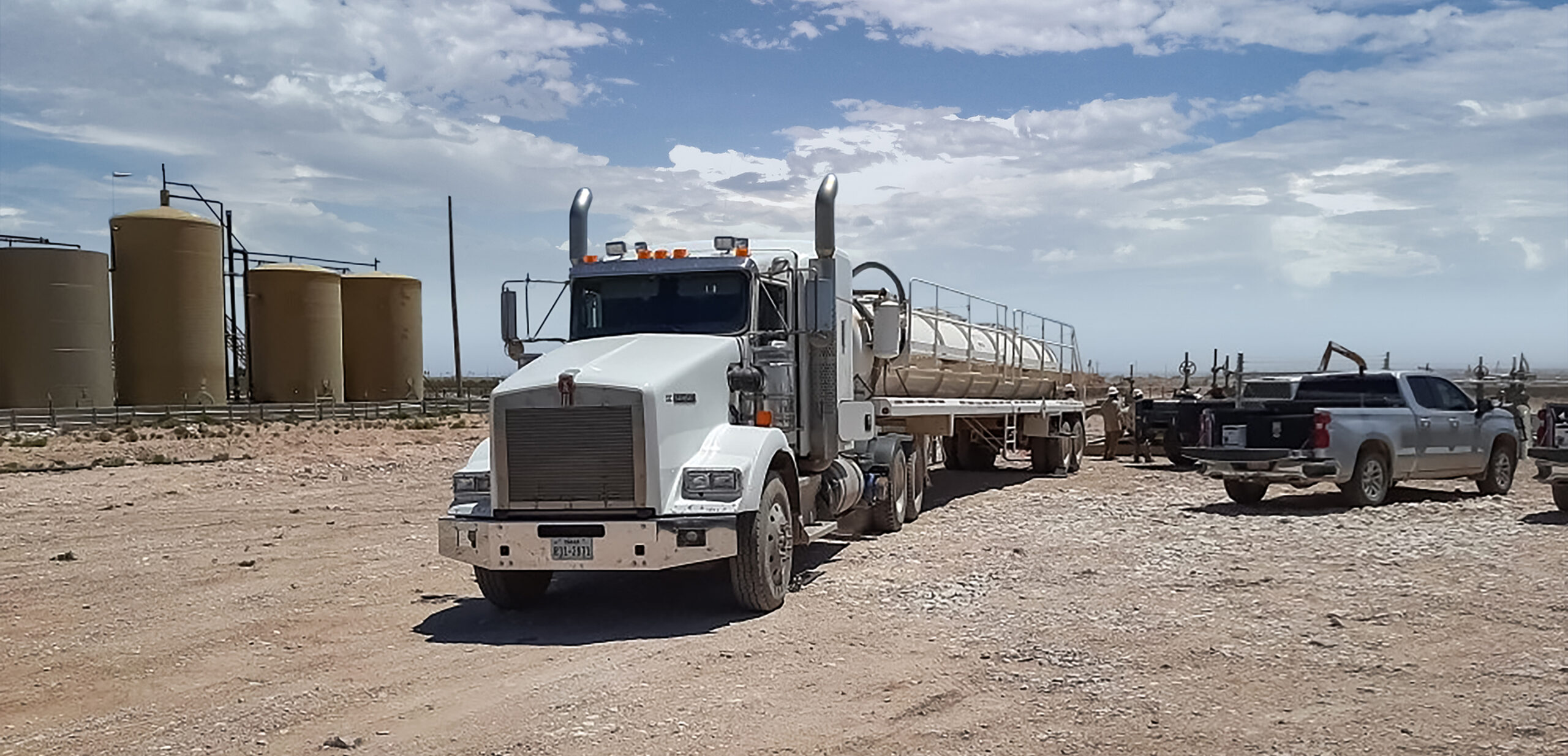 A truck is parked in the dirt near a gas tank.