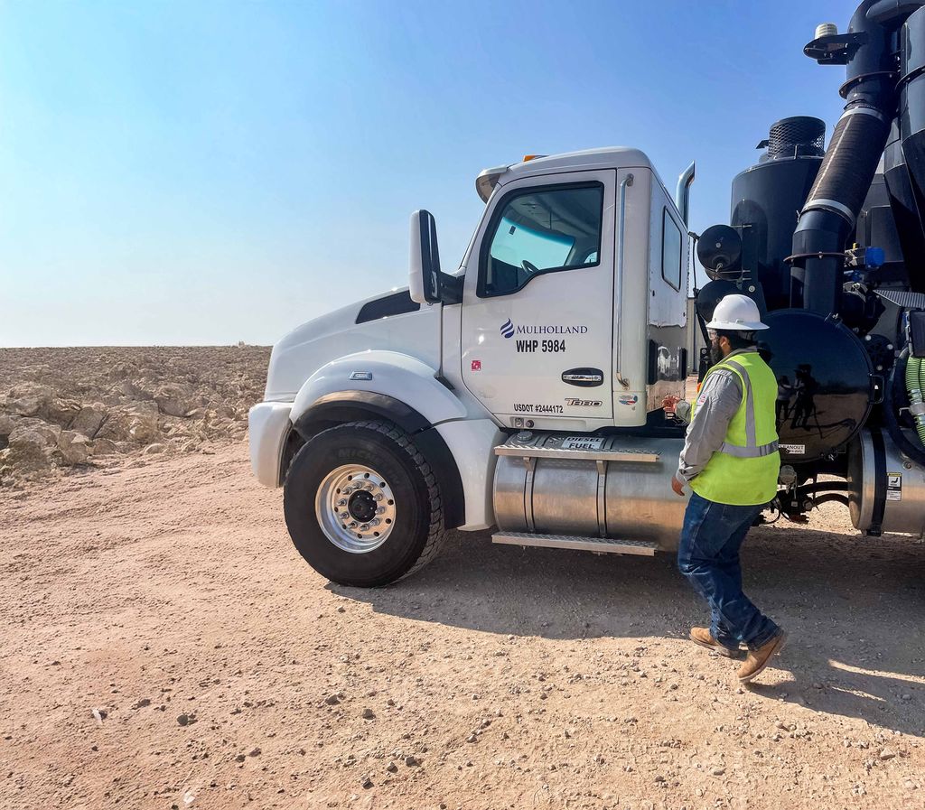 A man standing next to a large truck in the desert.