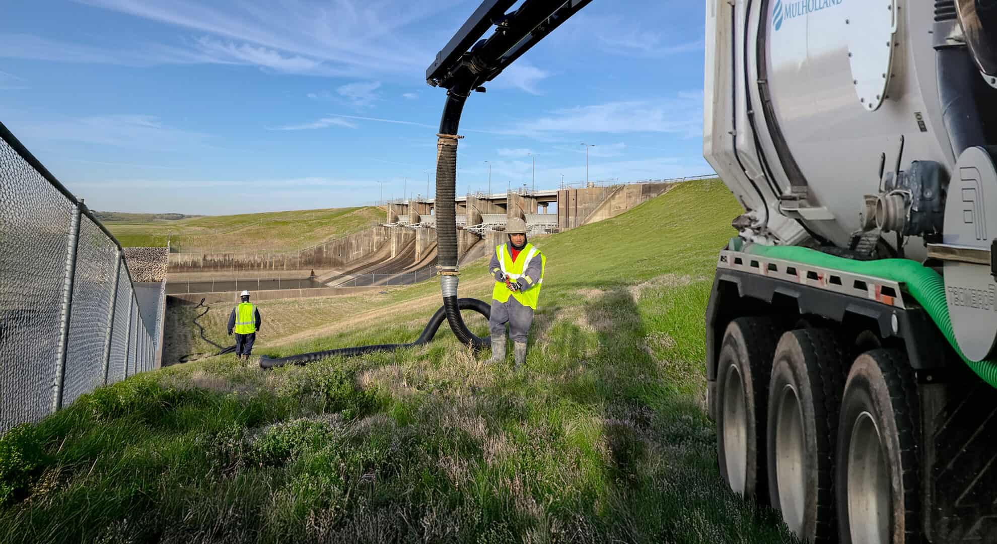 A man in work clothes is standing next to a truck that is being used to clean up a green field.