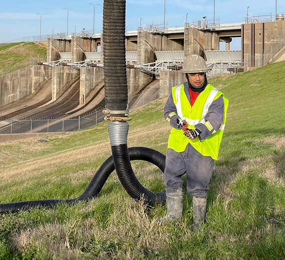 A man in a green safety vest standing next to a large pipe.