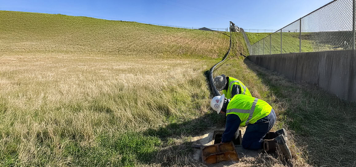Two men in safety vests working on a pipe.